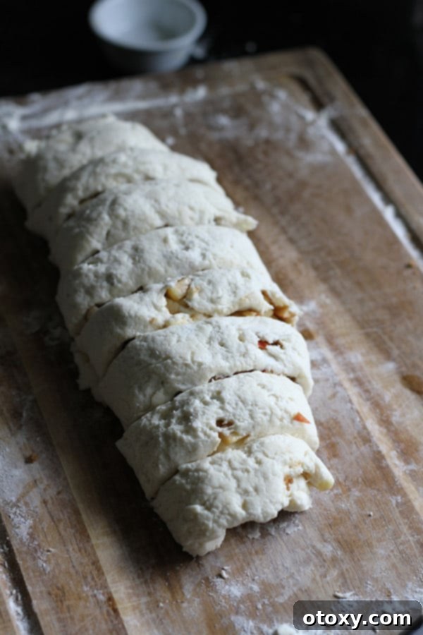 Air Fryer No Rise Apple Cinnamon Rolls 8 The apple cinnamon roll log being sliced into individual rolls on a wooden cutting board, revealing the beautiful spirals of dough and filling.