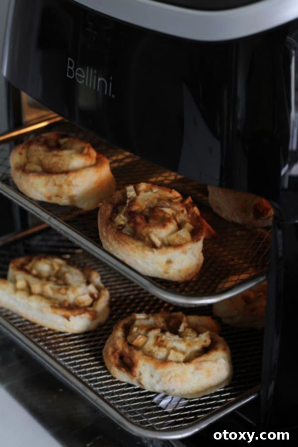 Air Fryer No Rise Apple Cinnamon Rolls 10 Golden brown apple cinnamon rolls actively cooking in an air fryer basket, steam gently rising.