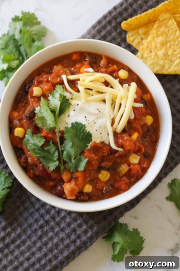 Triple Bean Vegetarian Chili 2 vegetarian three bean chili in a white bowl topped with greek yoghurt, cheese and cilantro.