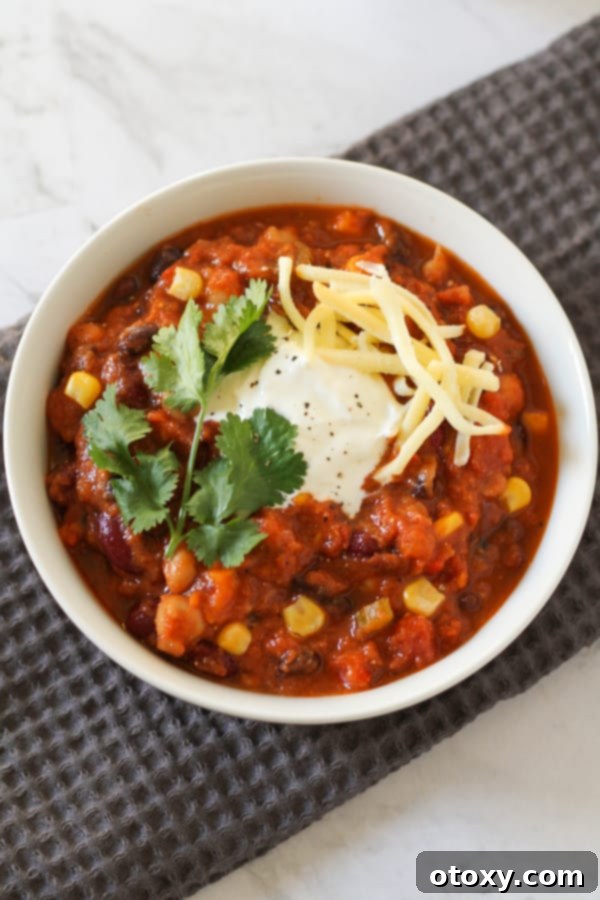 Triple Bean Vegetarian Chili 11 vegetarian three bean chili in a white bowl topped with greek yoghurt, cheese and cilantro.