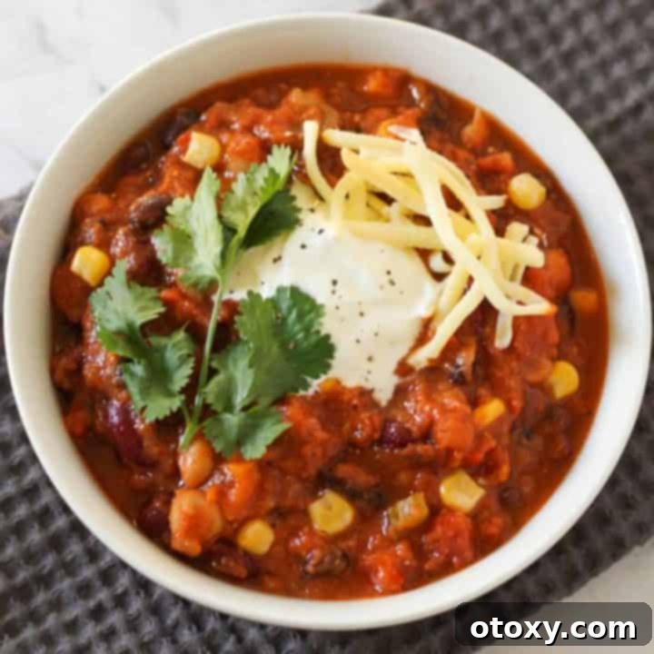 Triple Bean Vegetarian Chili 12 vegetarian three bean chili in a white bowl topped with greek yoghurt, cheese and cilantro.