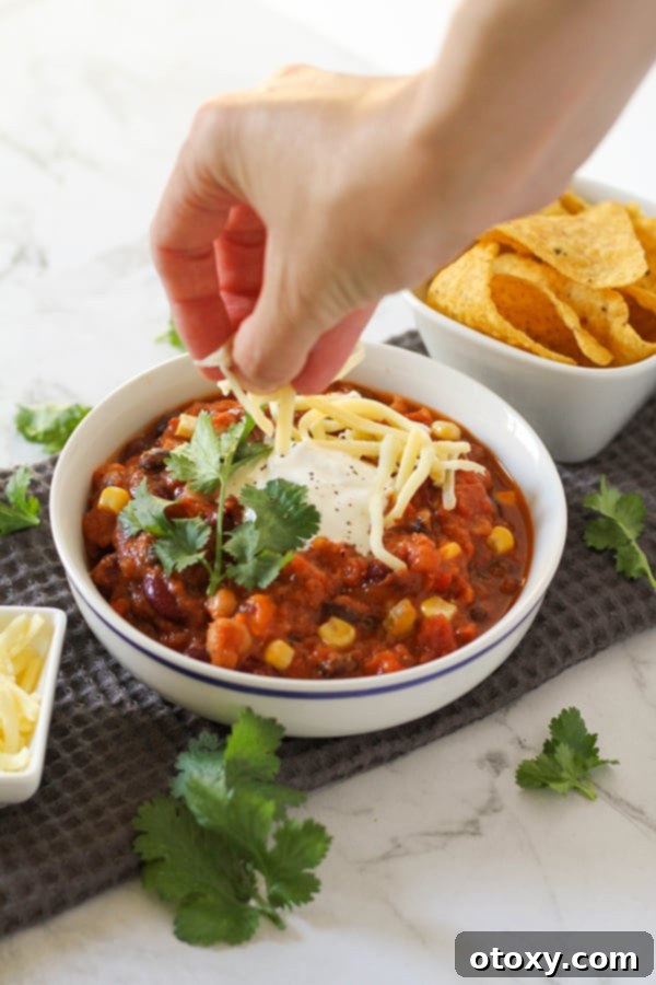 Triple Bean Vegetarian Chili 3 a hand placing shredded cheese on a bowl of vegetarian three bean chili.