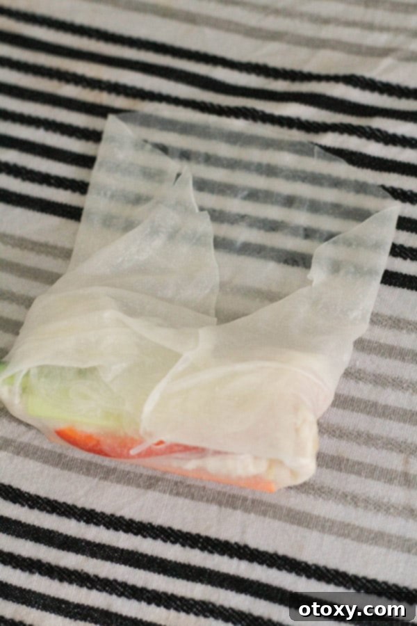 The next step in building rice paper rolls, showing how to fold the sides and roll tightly.