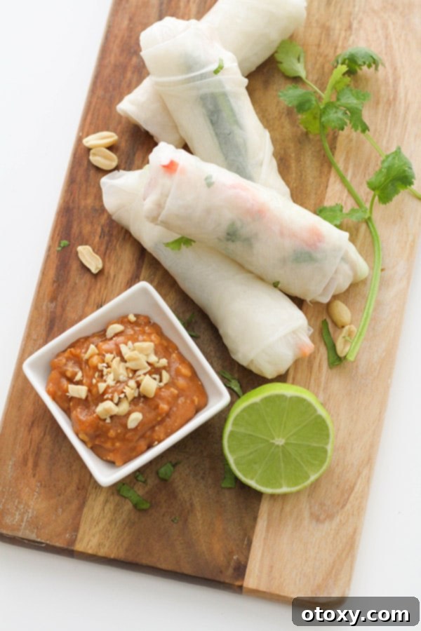 A small square white bowl of creamy peanut hoisin sauce, presented on a wooden board alongside freshly made chicken rice paper rolls.