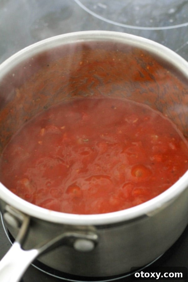Rich homemade tomato sauce simmering gently in a saucepan, vibrant red and aromatic, ready to be incorporated into the pasta dish.