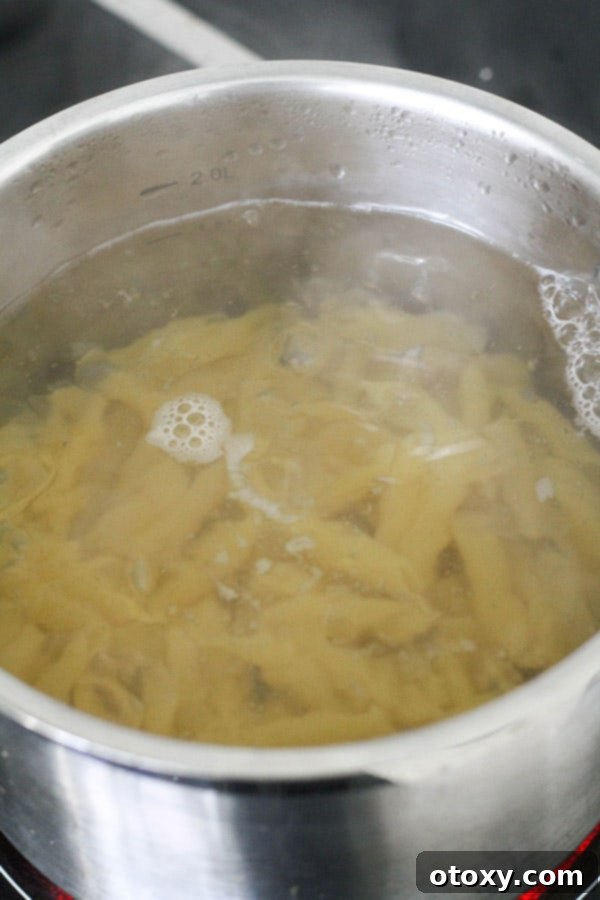 Penne pasta cooking in a large pot of boiling water, steam rising, a crucial step for achieving perfect al dente texture.