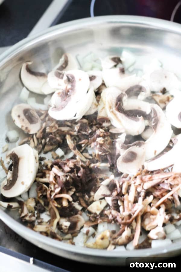 Sliced mushrooms and diced onions sizzling and caramelizing in a large frying pan, releasing their aromatic flavors, a key step to building the dish's depth.