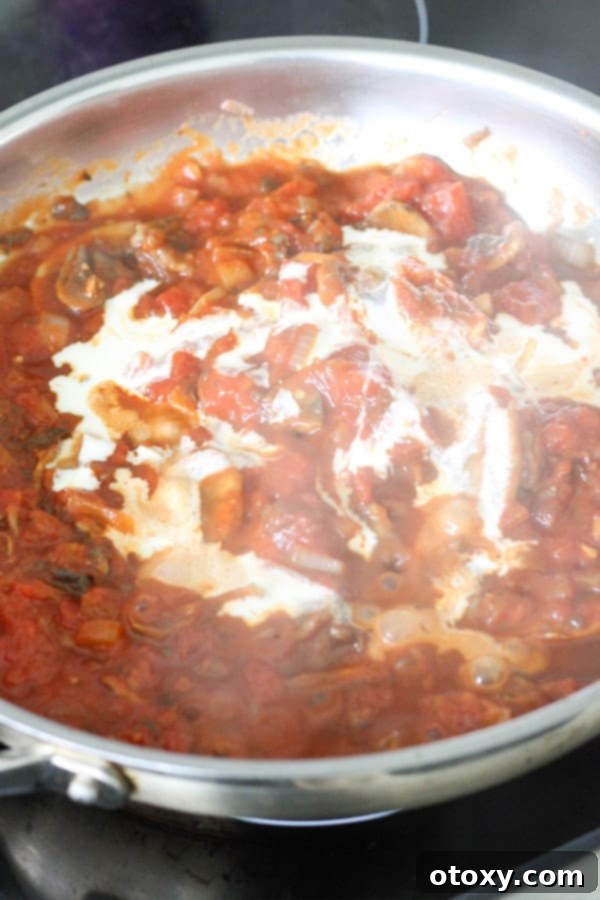 Rich homemade tomato sauce and heavy cream being poured into a large frying pan, creating a creamy and vibrant base for the pasta.