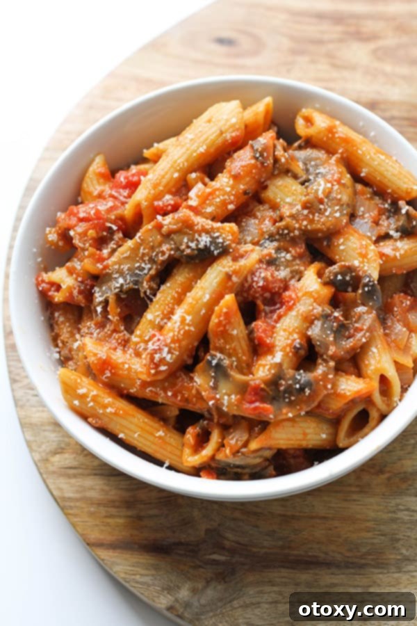 A close-up of a finished bowl of creamy Tomato Mushroom Pasta, garnished with fresh basil, showcasing the rich sauce and perfectly cooked pasta.