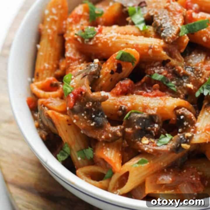 Close-up image of the finished Creamy Tomato Mushroom Pasta in a white bowl, garnished with fresh basil.