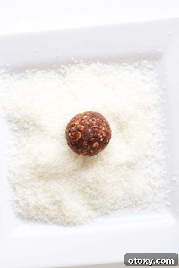 a chocolate coconut energy ball being rolled in shredded coconut on a white plate.
