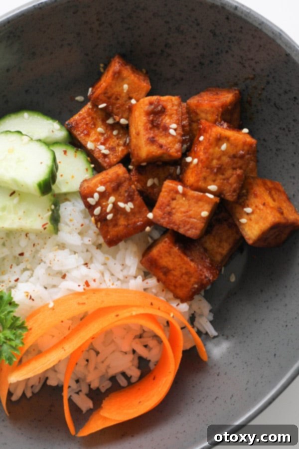 Cubes of golden pan-fried sriracha tofu on top of a bed of fluffy white rice, garnished with fresh green onions and sesame seeds.