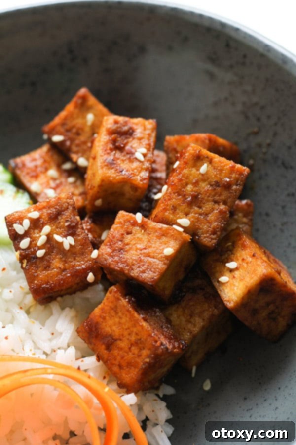 Close-up of perfectly browned cubes of sriracha tofu, glistening with sauce.