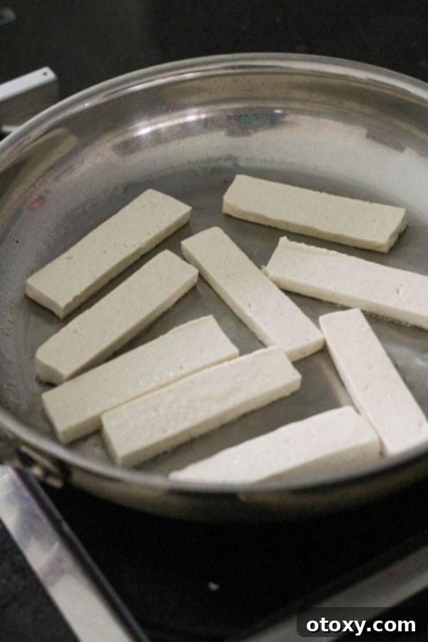 Tofu slices sizzling and browning in a hot frying pan with olive oil.