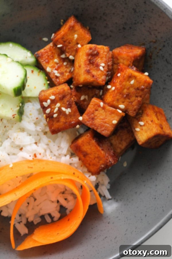 A close-up of a serving of pan-fried sriracha tofu cubes on rice, garnished with green onion, ready to be enjoyed.